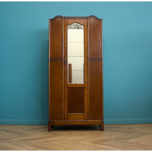 A 1930s oak wardrobe with a single mirrored door. The front features carved detailing. The base includes a full-width...
