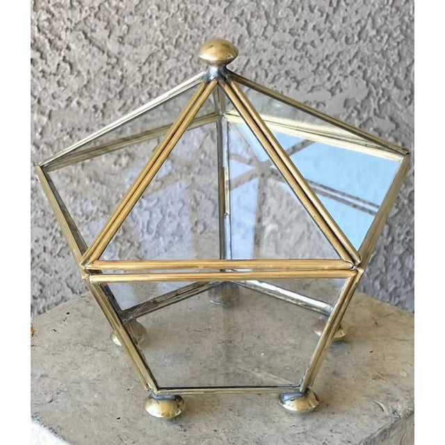 Stylish brass and clear glass pentagon-shaped keepsake or trinket box resting gracefully atop five bun shaped feet. There...