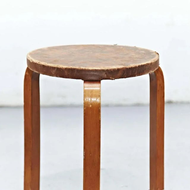 Stool designed by Alvar Aalto, circa 1960. Manufactured by Artek, (Finland) Leather top, wood legs and structure. In great...