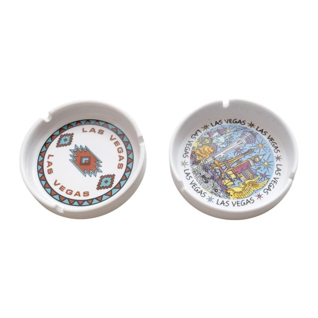 A pair of white ceramic Las Vegas souvenir ashtrays. One is a Hilton ashtray with a southwestern style design in teal and...