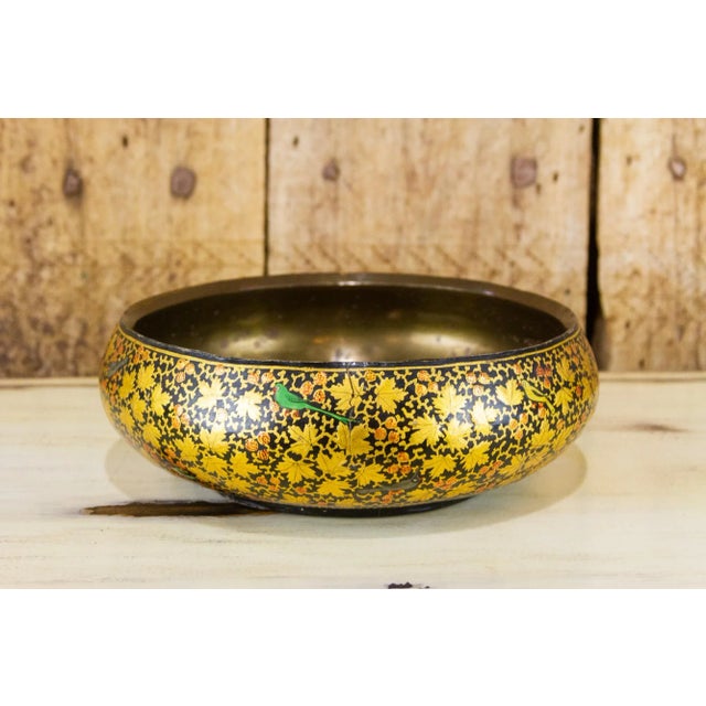 A decorative hand-painted paper mache bowl finished with a brass lining. The outer surface of the bowl is painted with...
