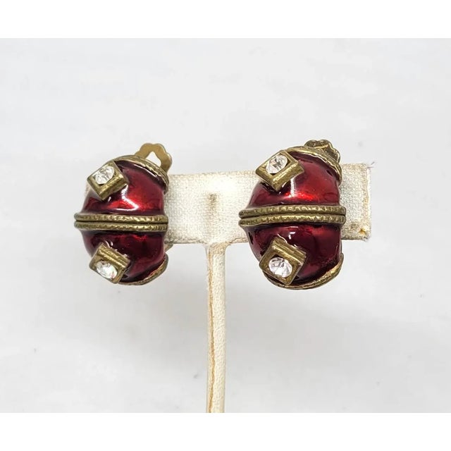 This is part of Chairish’s Costume Jewelry assortment. 1980s goldtone red enamel with round clear rhinestones half hoop...