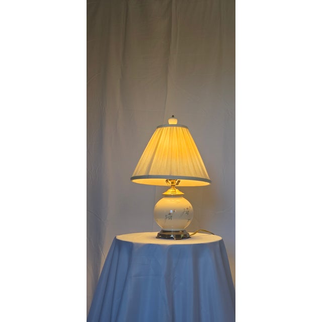 Elegant matching pair of vintage porcelain table lamps featuring softly rounded ivory-colored bodies adorned with delicate...