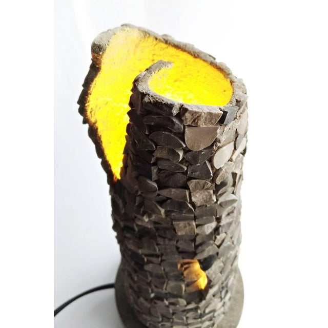 MEIR is a table lamp entirely handmade realized with fibreglass mesh to which dark and light gray cut pebbles have been...