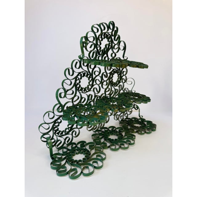 Vintage green metal display stand with three stepped levels and an intricate arrangement of oversized curls and circular...