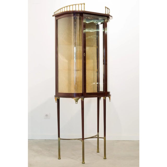 Semicircular single-section display cabinet, made of mahogany with brass trim and crown molding. A single door opens onto...