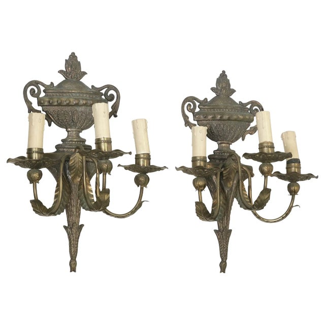 A refined pair of Italian Louis XVI style three-light wall sconces featuring classical urn-form crowns, scrolling arms,...