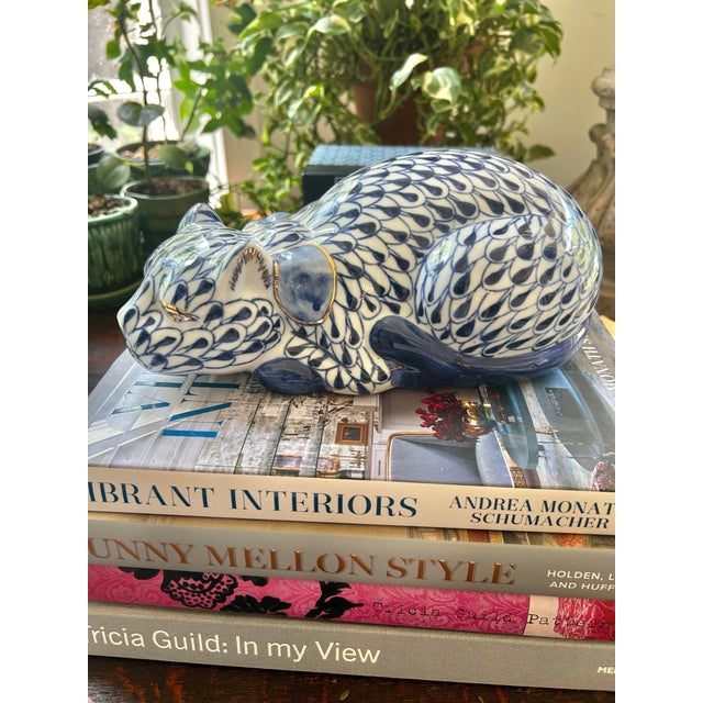 A charming hand-painted porcelain cat rendered in a classic blue-and-white fishnet pattern inspired by traditional...