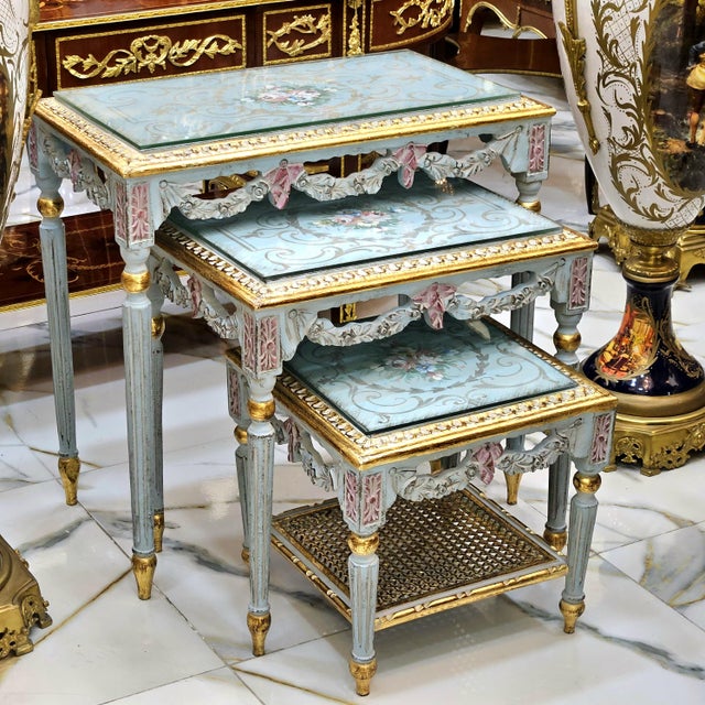 Elegant set of three French-style nesting tables featuring a beautiful soft sky blue finish accented with luxurious gold...