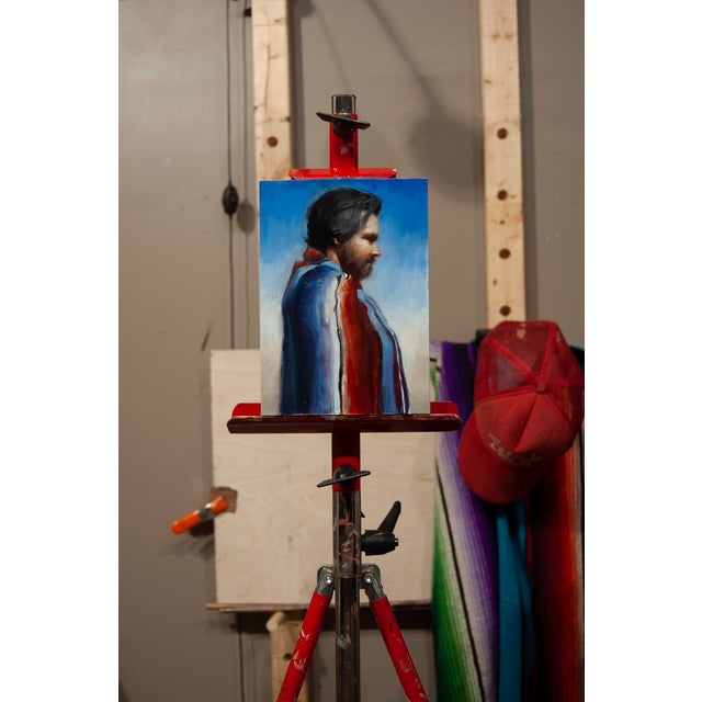 This oil painting features a profile of a man draped in a vibrant blanket, characterized by bold red, white, and blue...