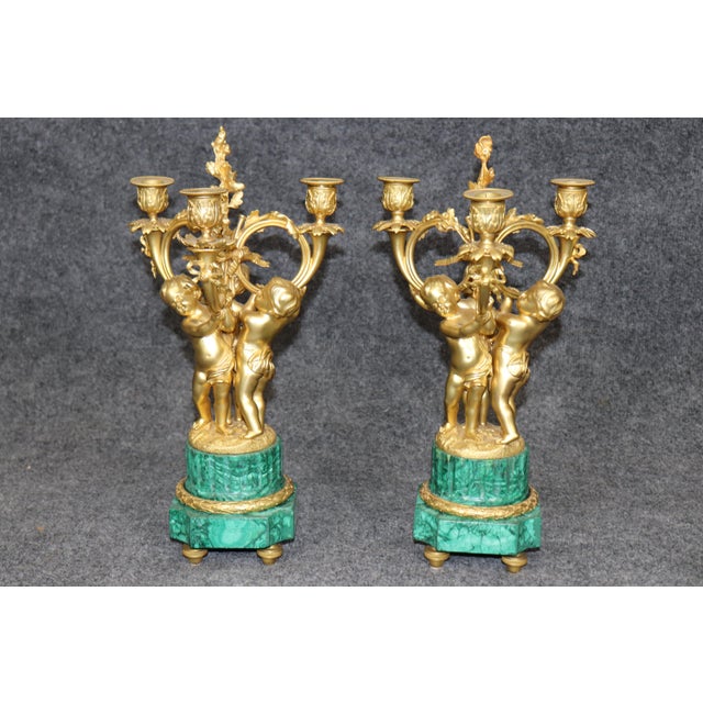 An exceptionally decorative French gilt-bronze and malachite three-piece clock garniture, conceived in the grand tradition...