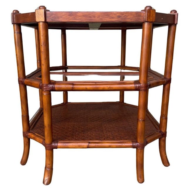A late 20th century American three-tier octagonal side table with a faux bamboo frame, one glass shelf and two woven...