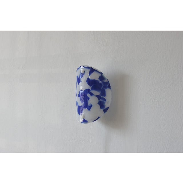A wall sconce with an organic form, made of decorative art glass with an irregular color pattern. The translucent pane is...