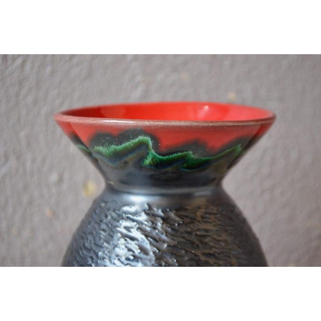 This ceramic, with its textured, bright red and black glazes, offers an interesting shape with its rounded body and open...