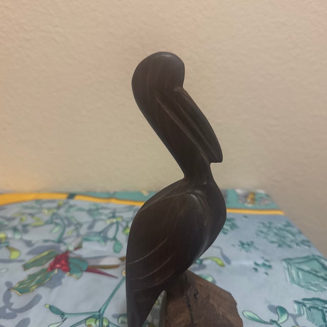 An expressive vintage hand-carved ironwood sculpture representing a coastal pelican perched on a rock. This piece features...