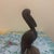 An expressive vintage hand-carved ironwood sculpture representing a coastal pelican perched on a rock. This piece features...
