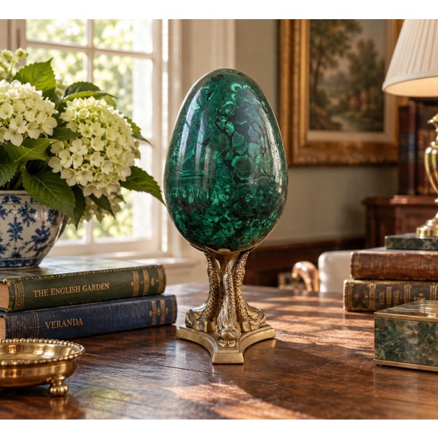 A beautifully proportioned malachite egg in richly veined shades of green and black resting on a neoclassical style brass...
