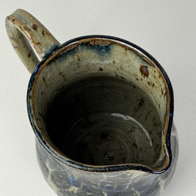 A beautiful hand made studio pottery pitcher with a unique oval shaped polkadots. They are in a deep blue against the gray...