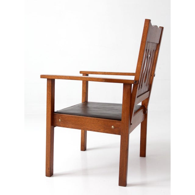 This antique Arts and Crafts armchair features a strong architectural form with wide flat arms, a stylized cutout splat...