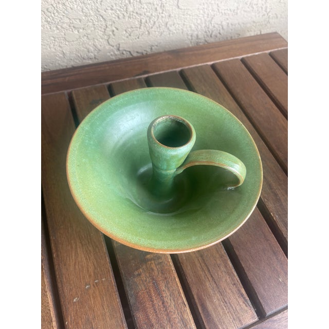 This item is a green glazed ceramic candle holder, specifically a style known as a chamberstick. It features a distinctive...
