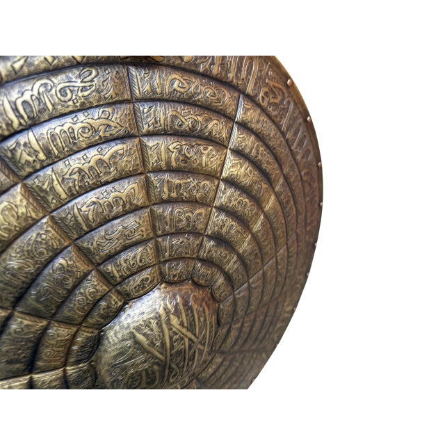 A striking display of technical metalwork and spiritual calligraphy, this heavy brass shield serves as a commanding focal...