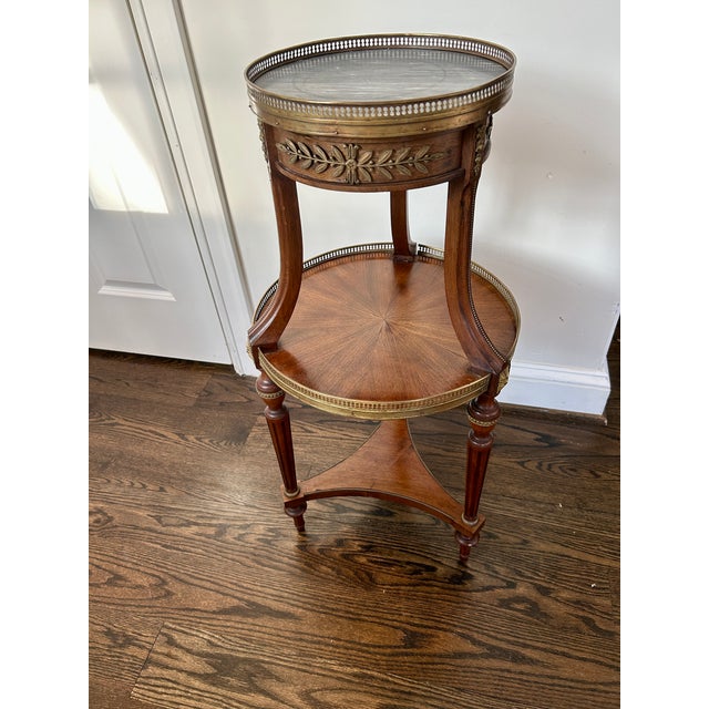 Elegant early to mid 20th Century French Louis XVI–style bouillotte table featuring a circular grey marble top set within...