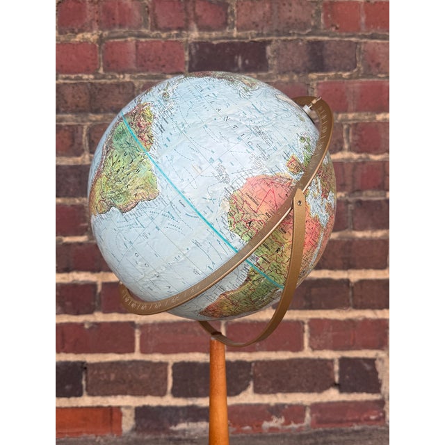 This vintage Replogle floor globe features a pristine globe mounted on a slender tapered wood pole situated on a brass...