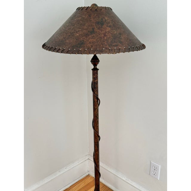 Arts & Crafts style wrought iron floor lamp on tripod legs with original shade. The lamp, shade, and finial all share the...