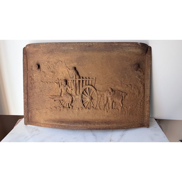 an antique cast-iron fireplace fireback featuring a raised relief scene of a horse-drawn cart with figures in a...