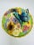 This is a vibrant ceramic dish with a lid, featuring detailed floral and butterfly motifs. The lid is adorned with...