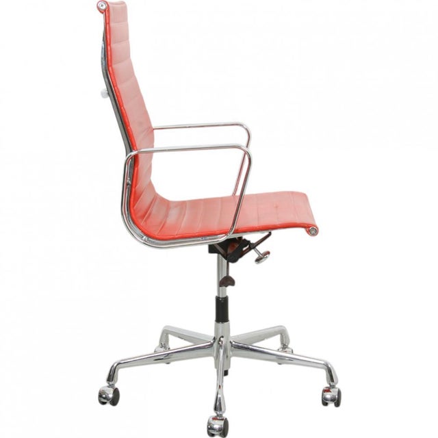 Charles Eames Ea-119 office chair upholstered in red leather, and with a chrome frame and chrome base. The chair appears...