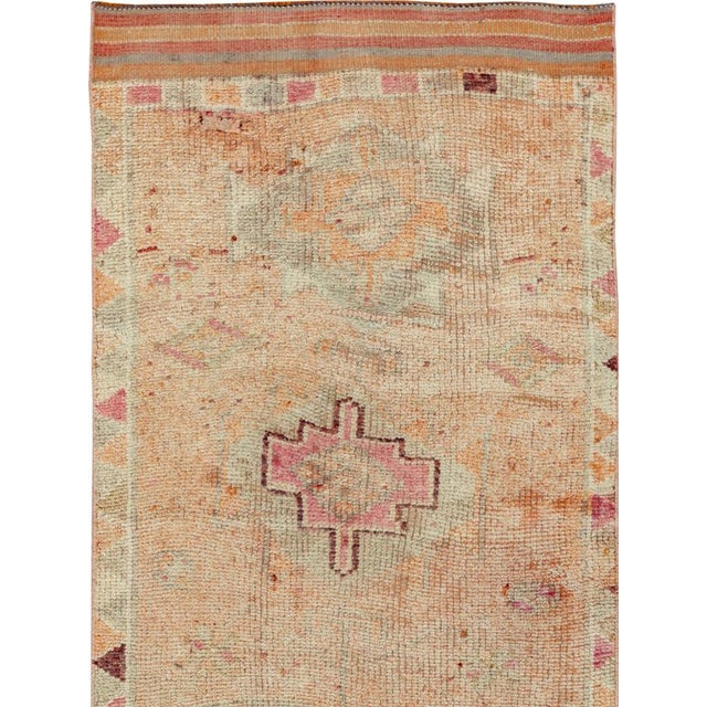 This mid-20th-century Turkish Anatolian runner presents a softly geometric composition arranged across a warm apricot,...