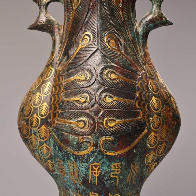 This decorative bronze vase features twin peacock‑form handles, intricately carved peacock feather patterns across the...