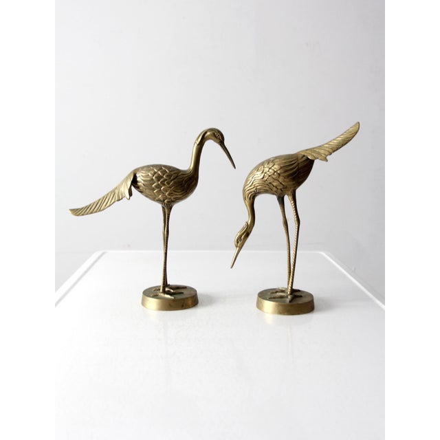 Pair of vintage brass crane sculptures featuring elegant silhouettes and detailed feather etching. One stands tall with an...