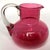 DETAILS An antique jug with a round cranberry glass body with straight neck and spout and applied clear glass C-shape...