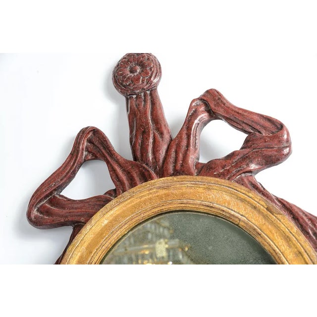 French Baroque style oval wall mirror. The mirror features a large bow and ribbon crowning the gilt mirror. A double iron...