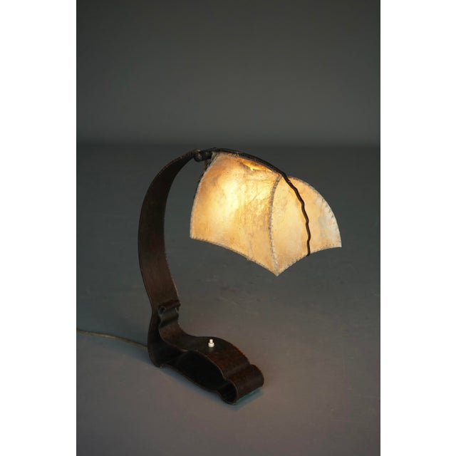 Hand-forged wrought iron desk lamp with original parchment lamp shade. The shade has a bit of heat damage to the top. The...