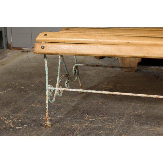 A French rustic, painted iron garden bench from the 19th century with scrolling motifs on the back, curving slatted seat...