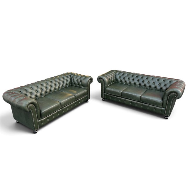 English Chesterfield sofas upholstered in rich dark green leather, featuring deep button tufting, classic rolled arms, and...