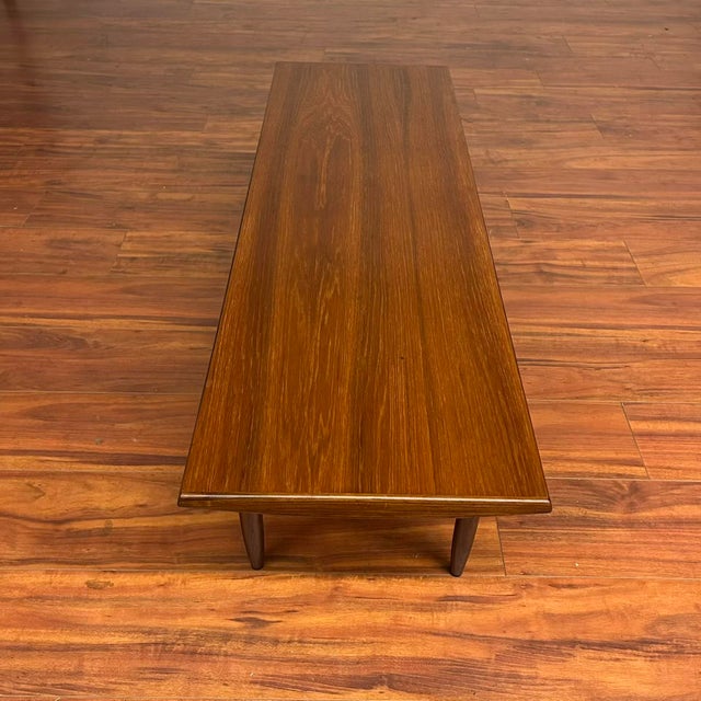 Vintage Danish modern teak coffee table with beveled edges and tapered legs with bowtie stretchers. It is a great size for...