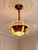 A distinctive Art Deco style pendant light combining warm amber tones with a broad decorative glass disc. The transparent...