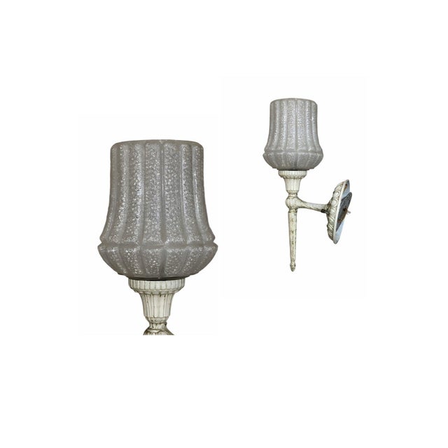 A charming vintage single-light wall sconce. Featuring a heavy textured clear glass shade paired with an ornate off-white...