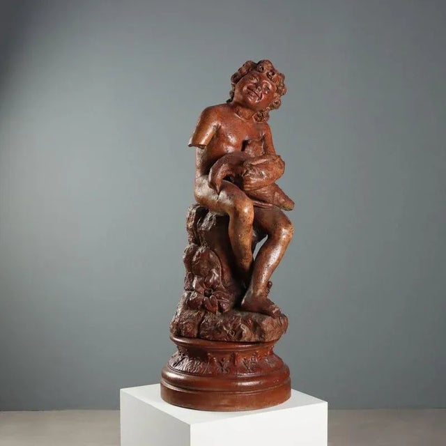 Patinated terracotta sculpture depicting a boy with a dove sitting on a stump. The statue is presented on a circular stand...