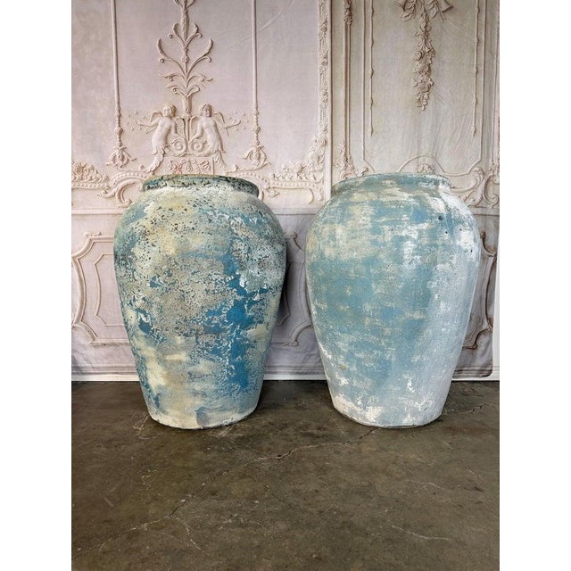 An impressive pair of oversized terracotta urns showcasing a richly weathered surface with traces of blue mineral patina....