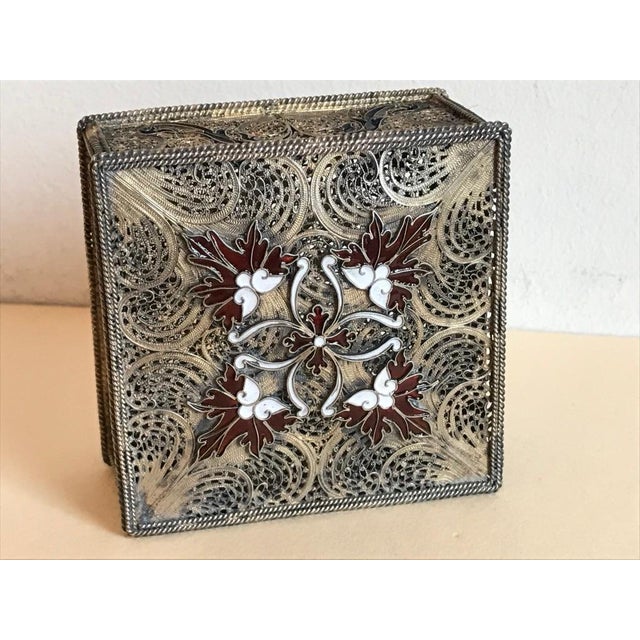 A silver trinket box with exquisite filigree work throughout, including the bottom and the feet. With white and red enamel...