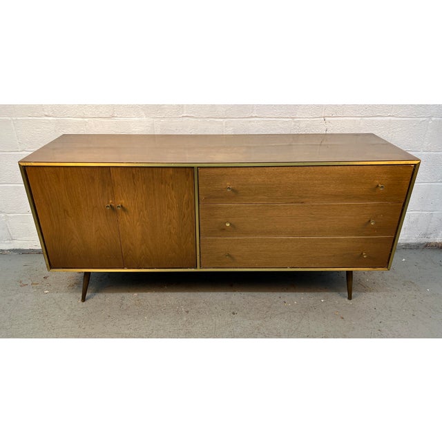 Beautiful mid-century modern walnut dresser featuring clean lines, tapered legs, and elegant brass-tone trim and pulls....