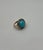 This elegant ring is crafted in a sophisticated design. It features a striking turquoise cabochon, encircled by a halo of...