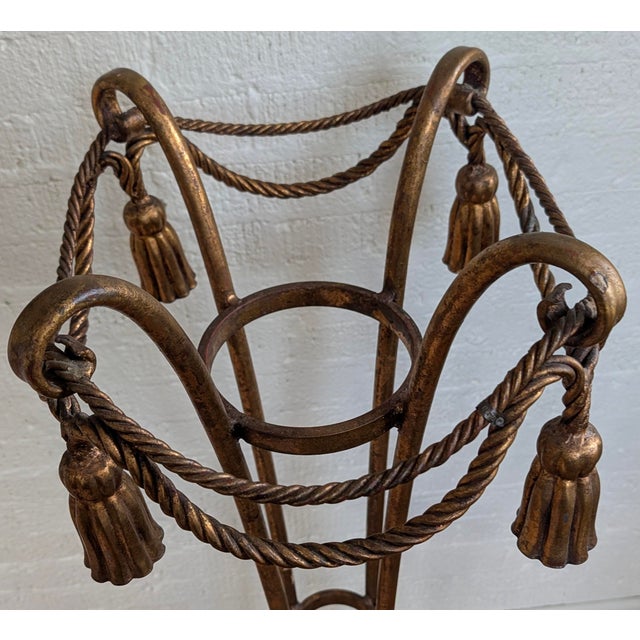 A striking vintage Hollywood Regency gilded iron fern stand featuring elegant rope swag and tassel detailing. Beautifully...