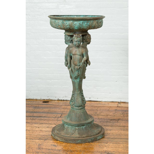 A Classical style bronze pedestal urn from the 20th century with three putti and verde patina, two available priced and...
