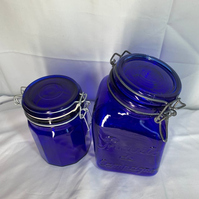 Offered here are vintage cobalt blue glass storage canisters featuring wire bail clamp lids and embossed lettering. One of...
